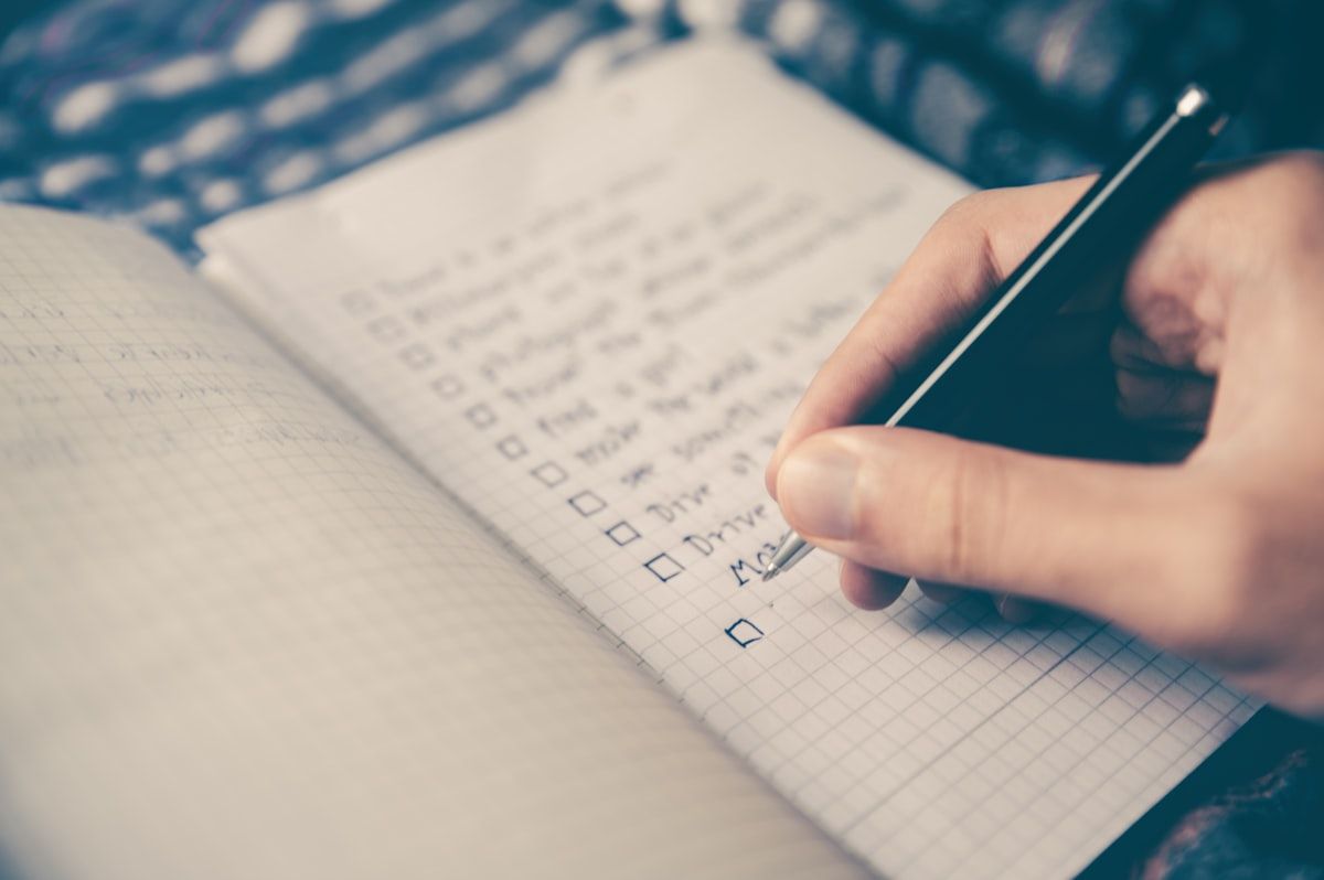 Hand with a pen ticking off a handwritten checklist in a grid-paper notebook